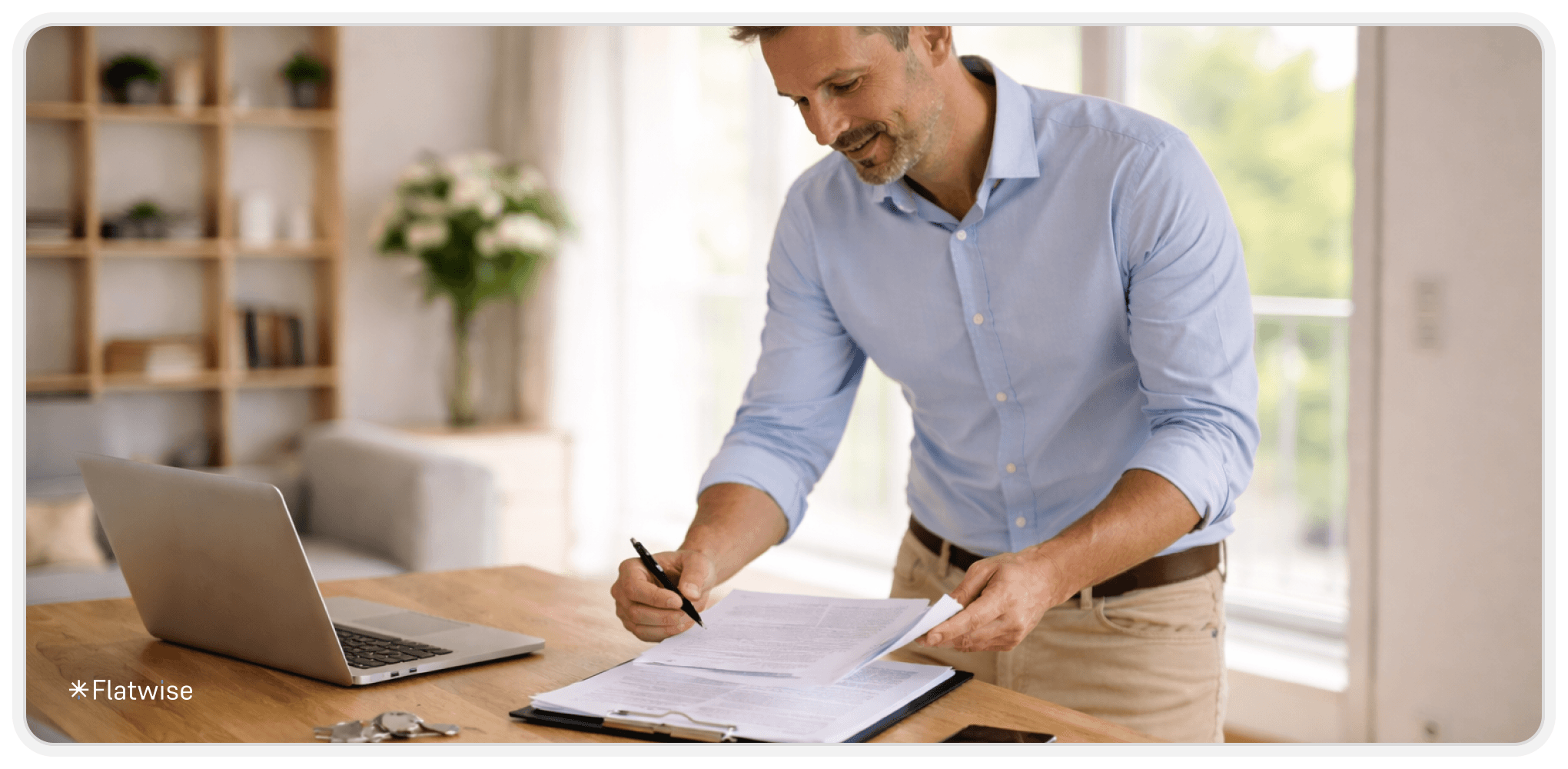 Esszimmertisch mit Laptop, Schlüssel und Handy. Mann mit Hemd schreibt auf Unterlagen