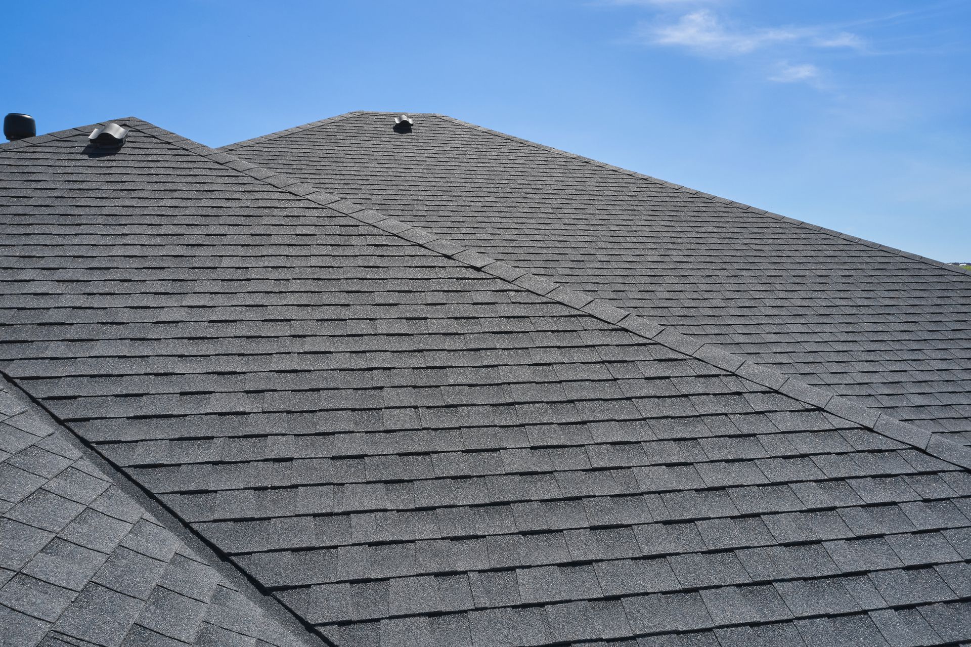 Close-up of a gray shingled roof with a prominent ridge cap against a clear blue sky.