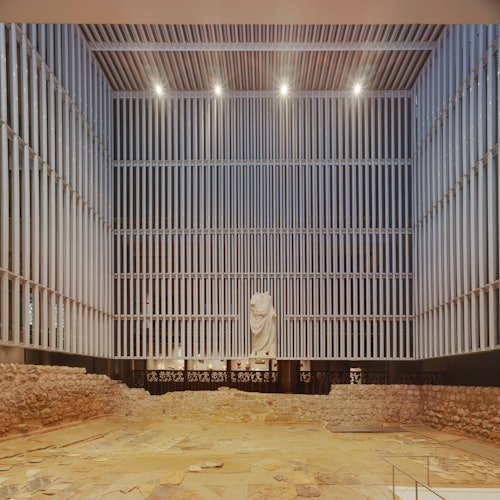 室内考古展览，展示古代遗迹和一座显眼的白色雕像，由天花板灯光照明。