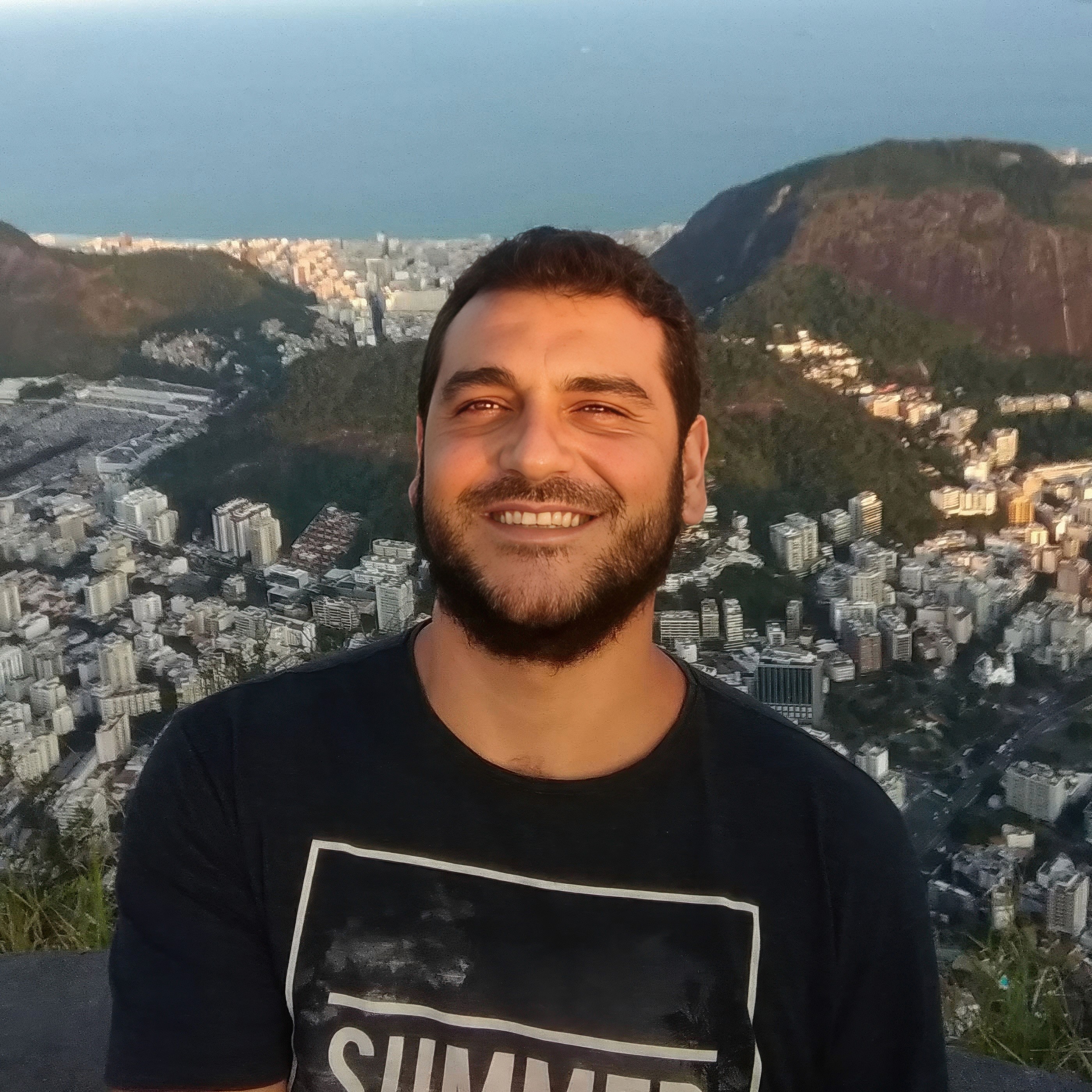 Close-up portrait of a person wearing a gray insulated hooded jacket with the hood up, showing their face framed by the hood against a light background.