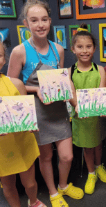 Older art class students posing with nature canvases they painted