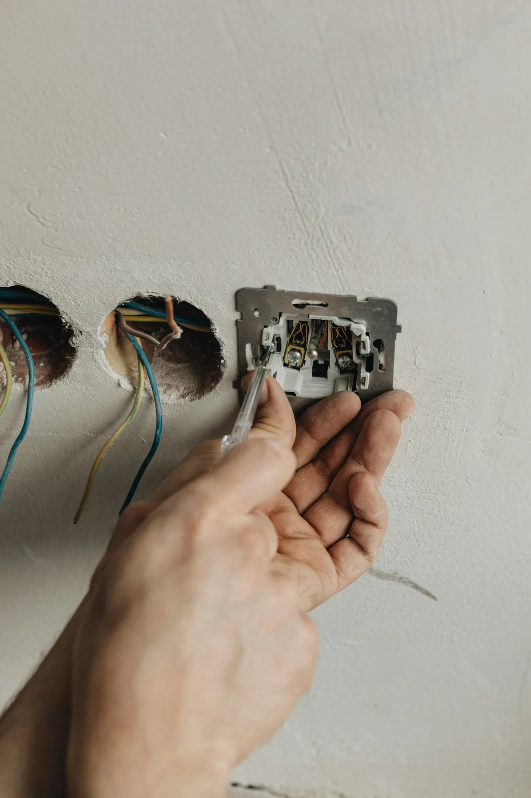 Electrician installing wall switch mechanism with screwdriver at outlets