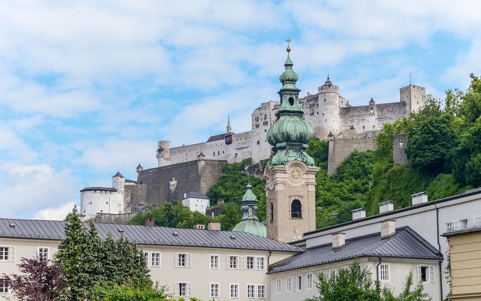 St Peters Abbey and Hohensalzburg Castle in Salzburg, Austria, with lush greenery.