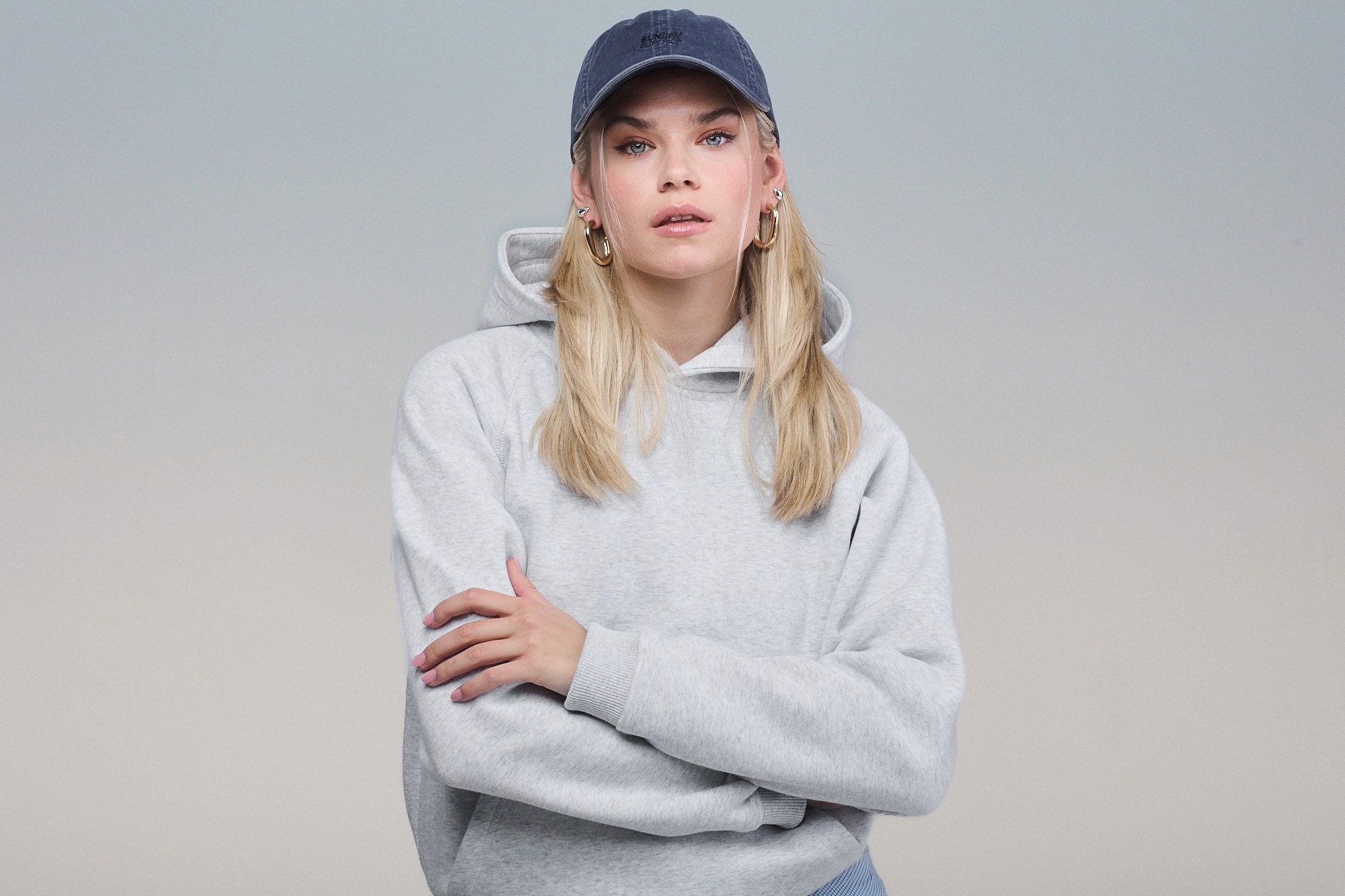 Woman wearing light grey hoodie and a washed cap