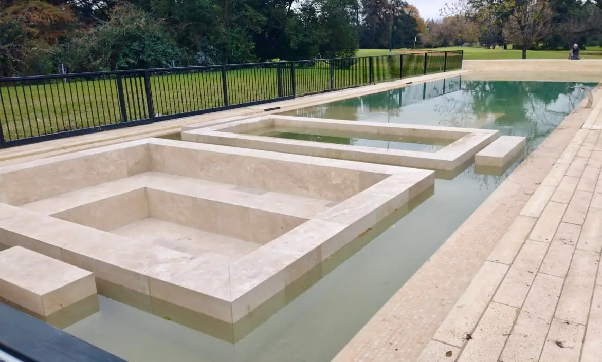 Amplia piscina de hormigón con múltiples sectores y solárium húmedo, revestida íntegramente en mármol travertino de primera calidad.