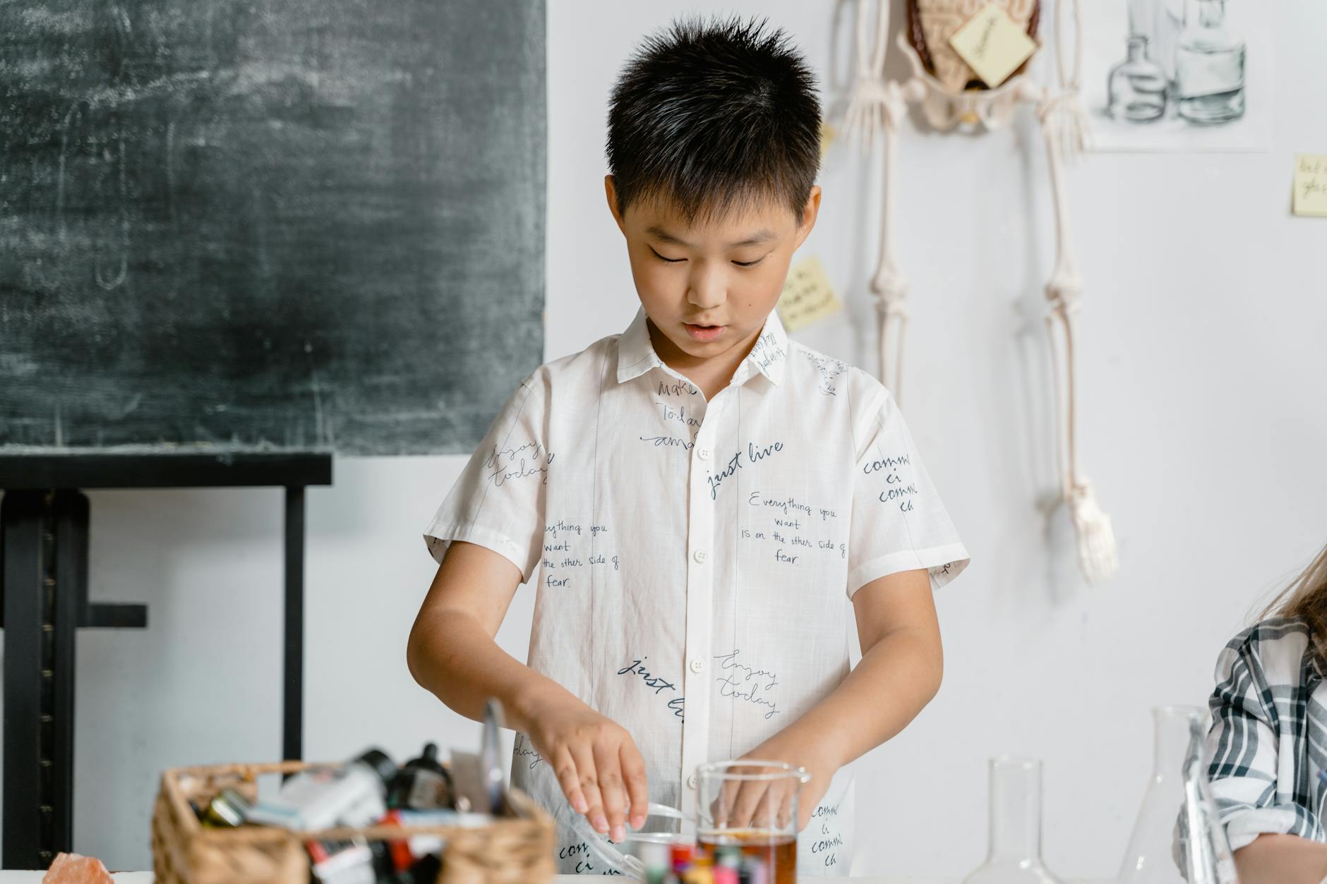 Close-up of a child using a magnifying glass to examine a leaf next to open STEM picture books on a wooden table.
