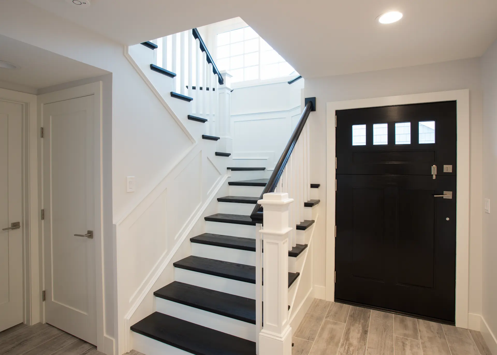 Elegant entryway with black-and-white staircase, skylight, dark wood door. From Dana Point Cape Cod remodel, photo by Chris Darnall.