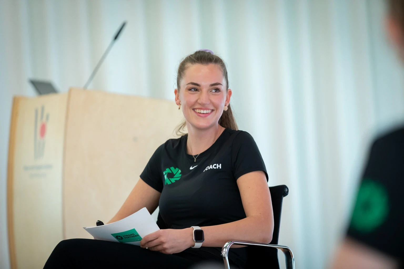 Strong Partners Coach sitzt auf einem Stuhl und hat Moderationskarten in der Hand