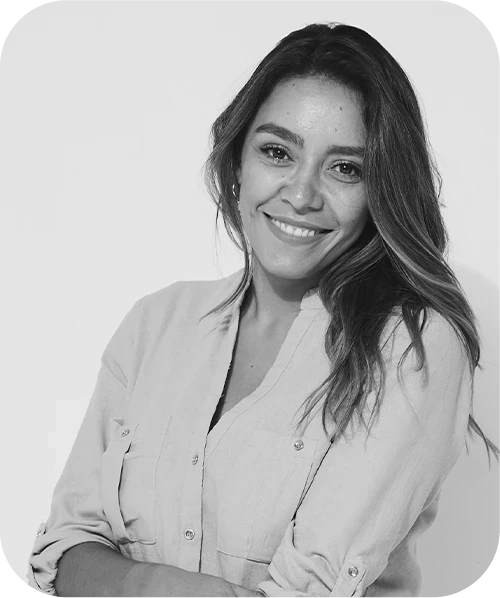 A woman with short, curly hair, wearing round glasses and a white t-shirt, smiling.