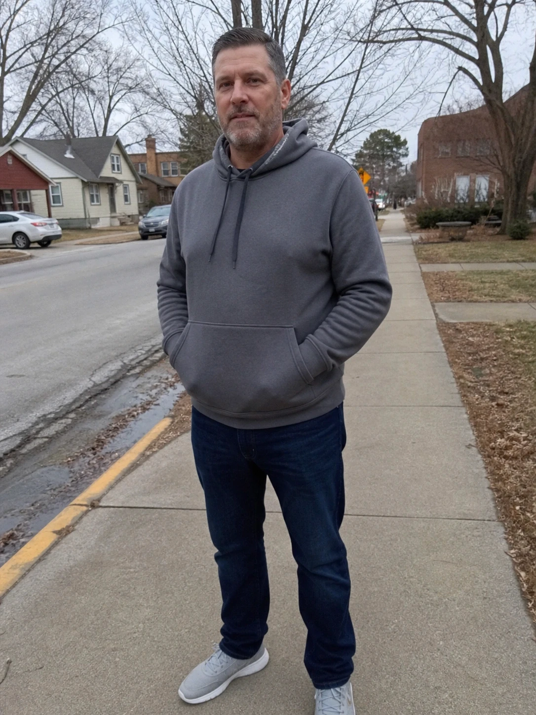 Man in gray hoodie standing on neighborhood sidewalk