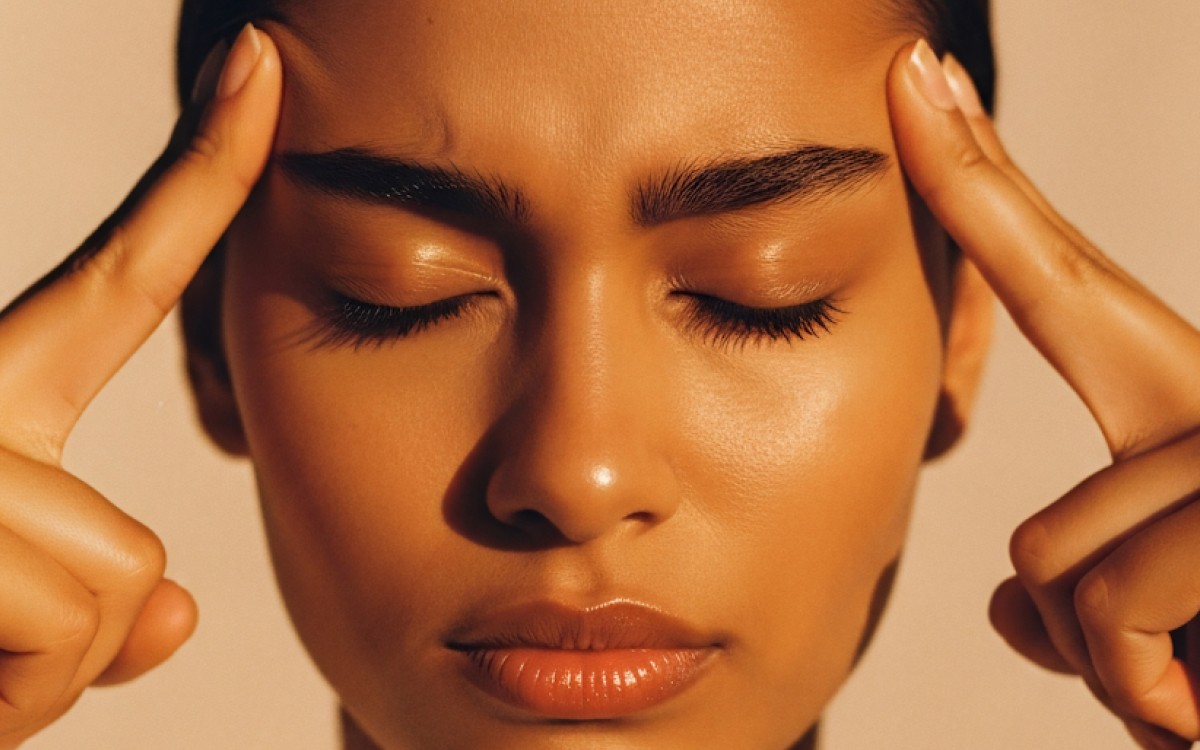 A person with closed eyes and a calm expression touches their temples with both index fingers, bathed in warm light, conveying serenity and focus.