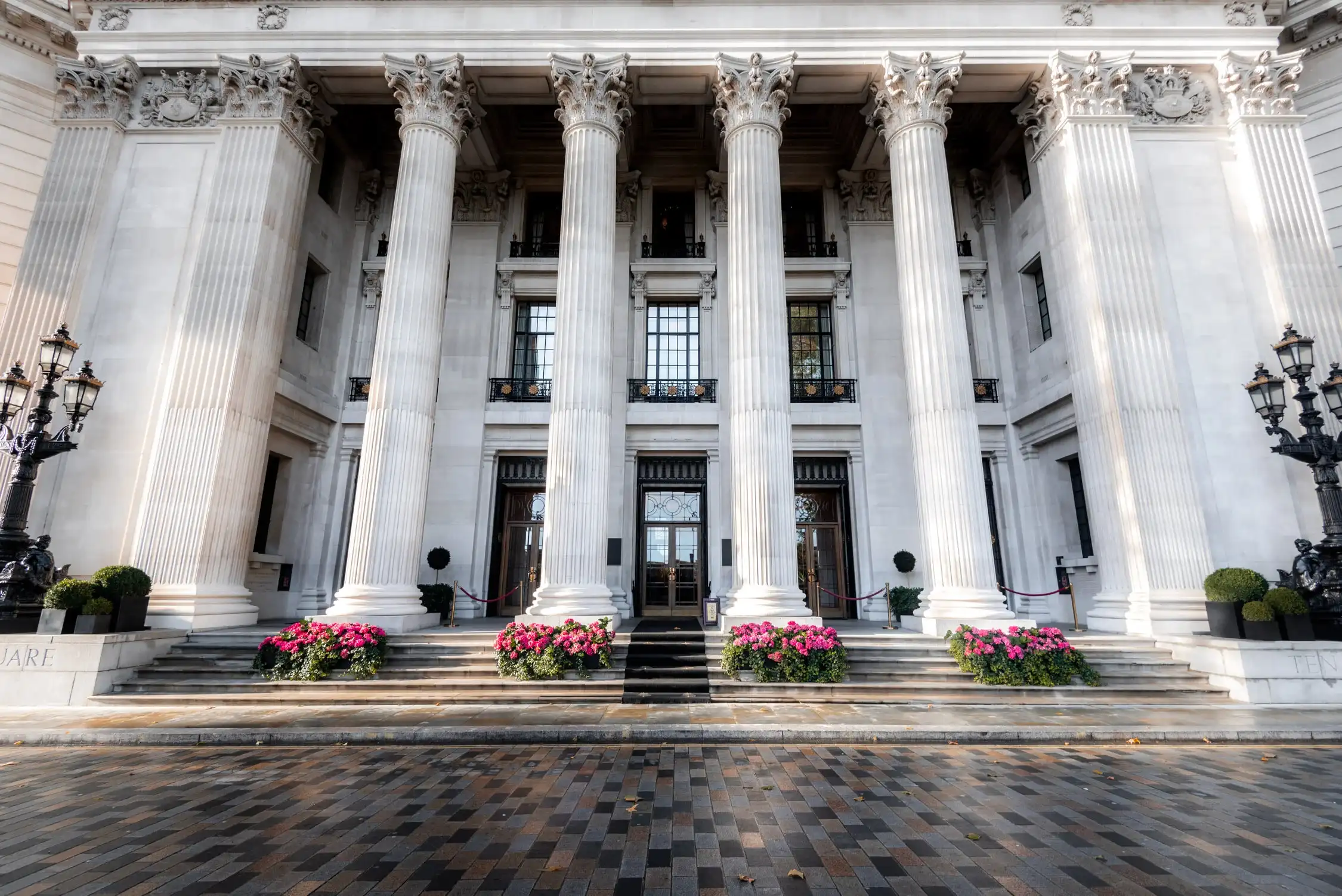 Neoclassical building with massive white columns and a grand entrance decorated with pink flowers at the base.
