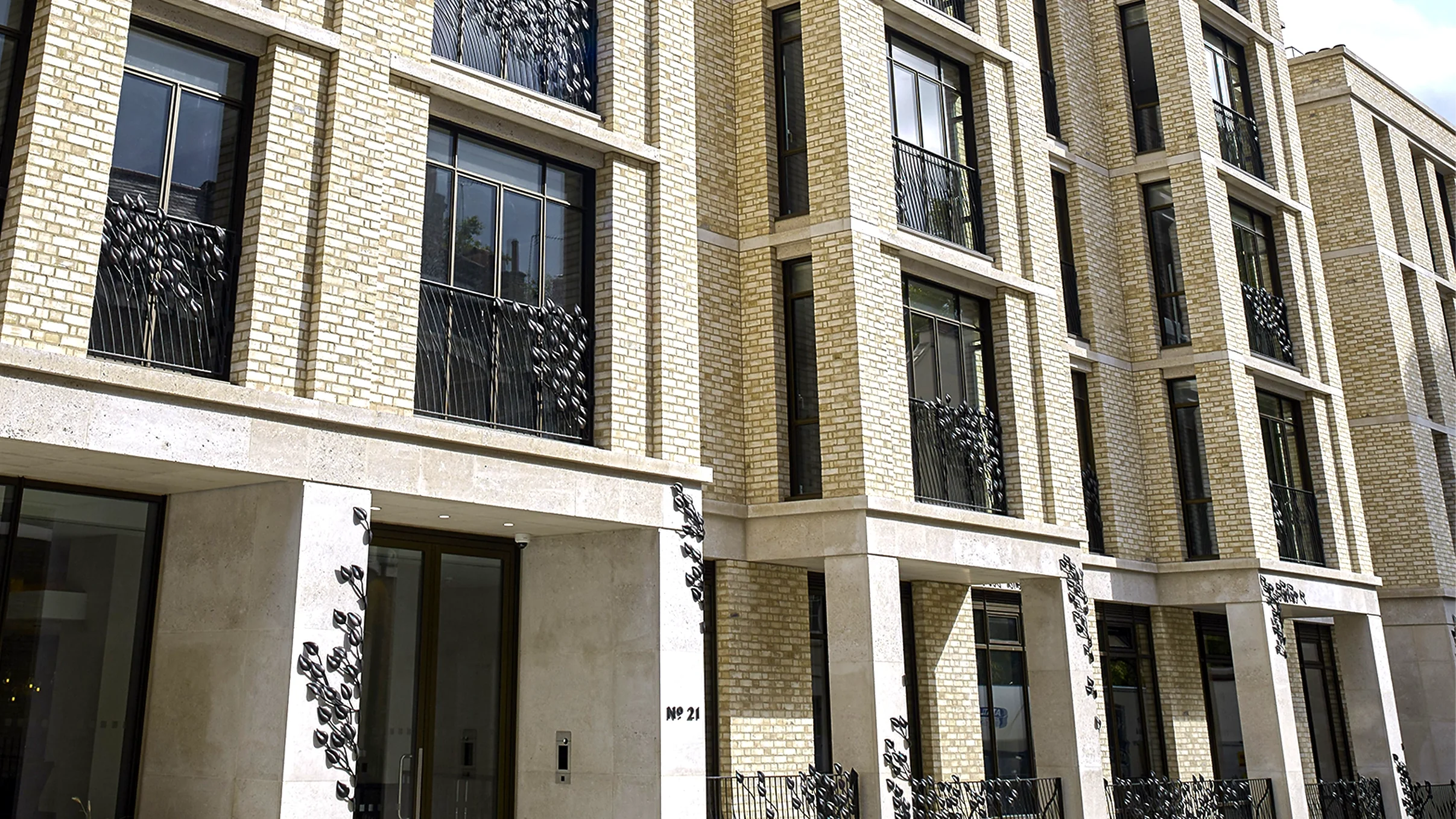 The exterior facade of a luxury cream-brick residential building featuring bespoke bronze balconies and leaf-motif decorative gates. An expansive architectural objet d’art project created by Shaun Leane's independent studio.