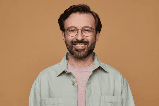 Smiling man with beard and round glasses in light green jacket.