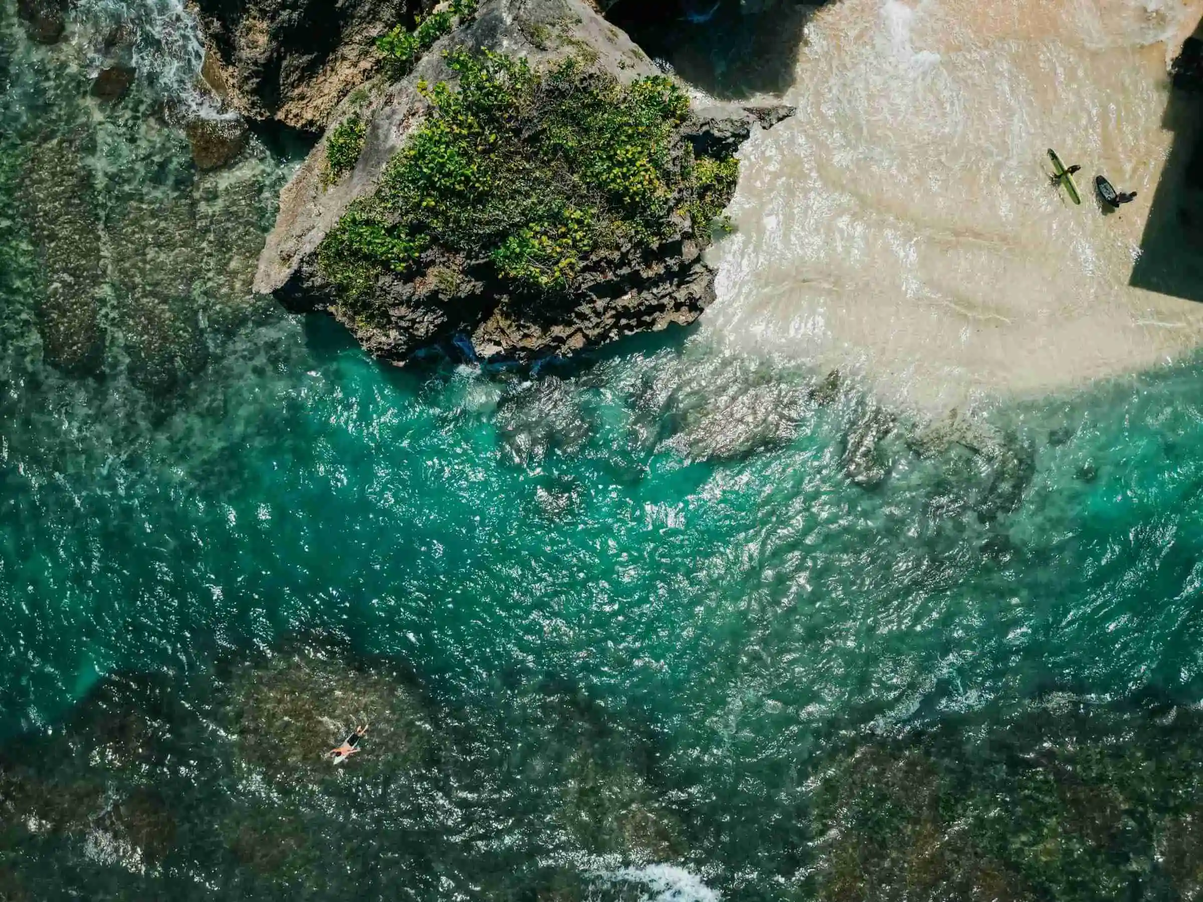 Aerial view of a stunning Bali beach and surfers, showcasing the tropical lifestyle of our multi-style yoga teacher training retreat