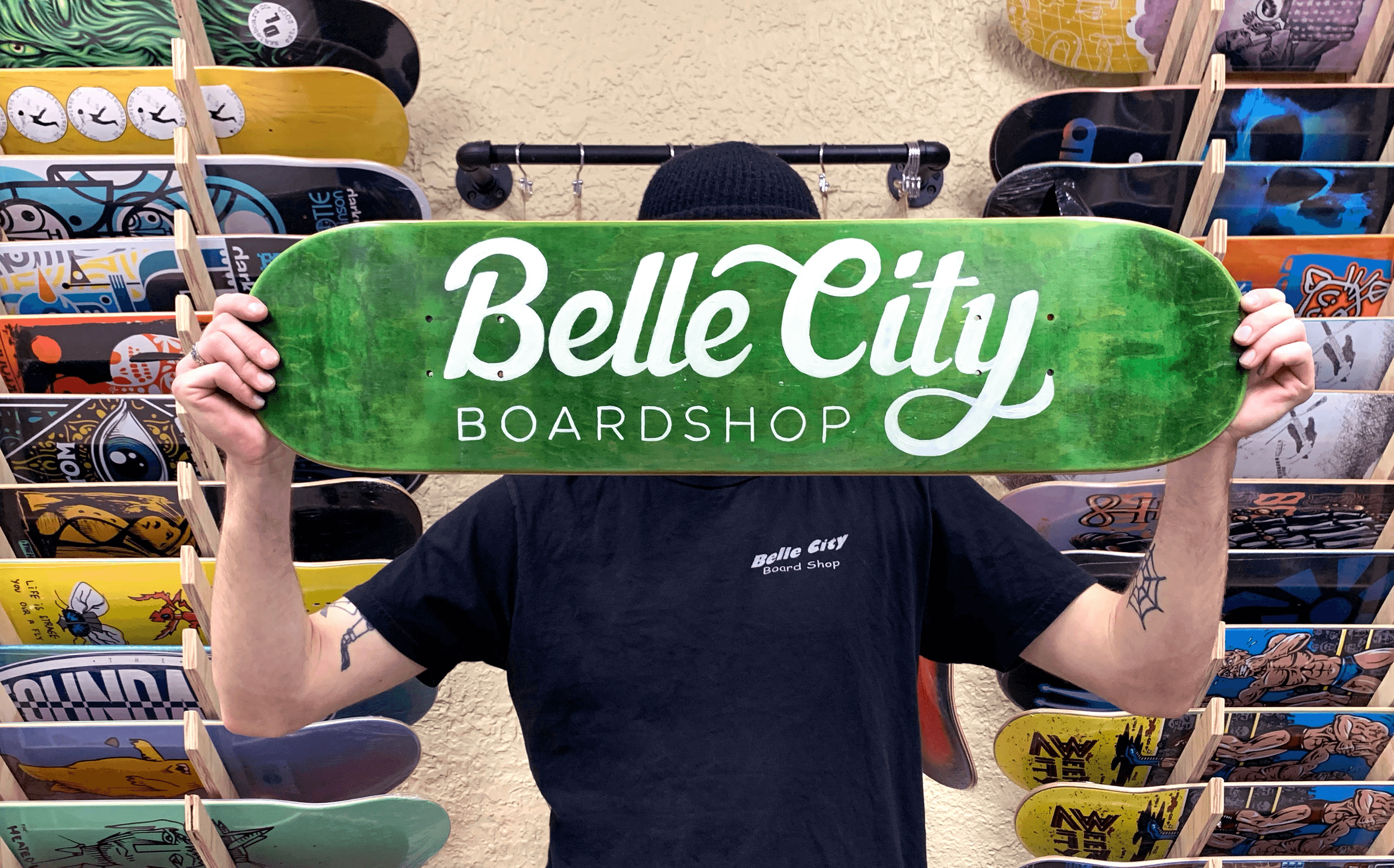 Man holding a painted skateboard that reads Belle City Boardshop