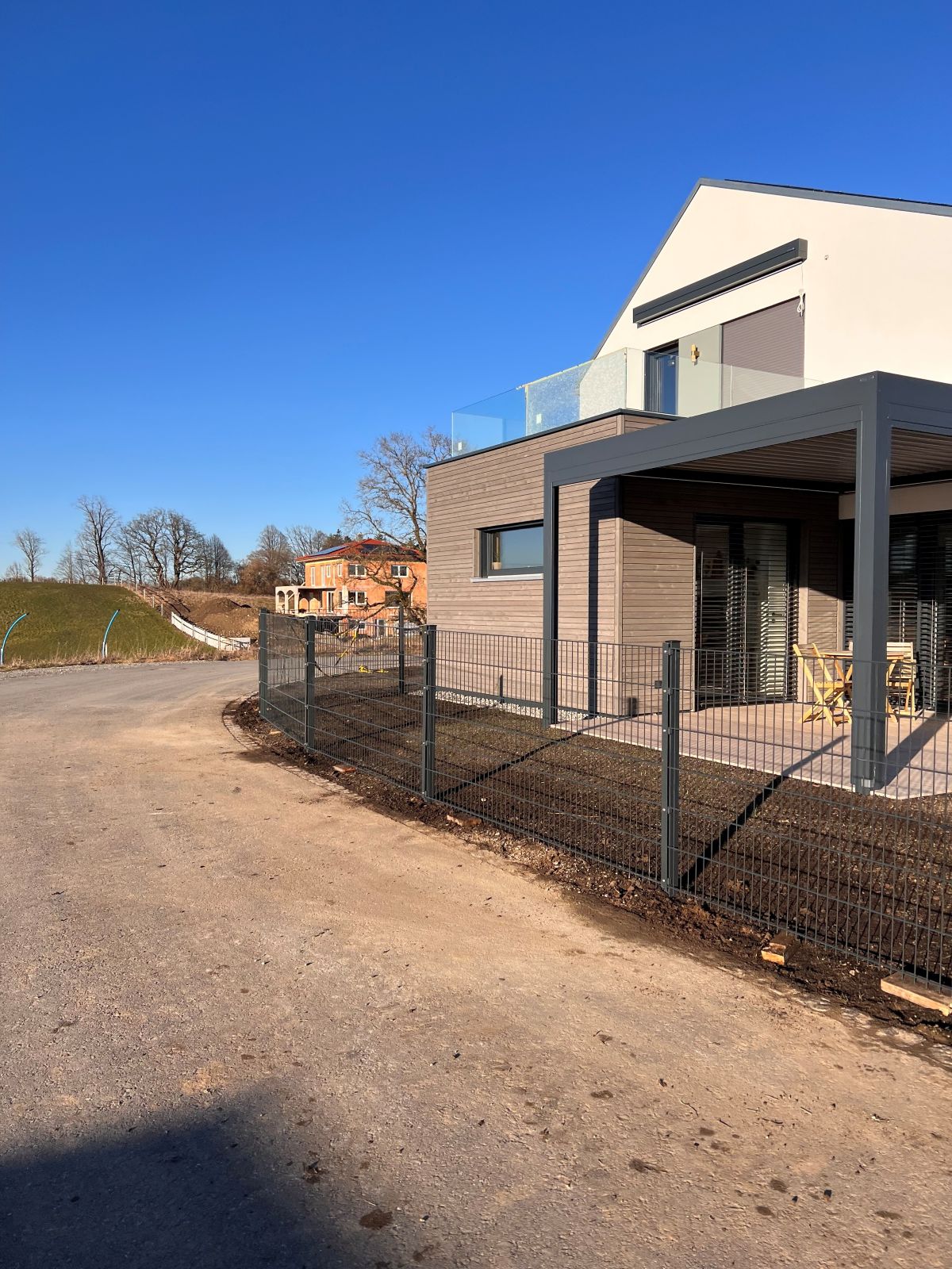 Installation eines modernen, dunkelgrauen Doppelstabmattenzauns an einem Neubau mit Holzfassade und Terrassenüberdachung, Gartengestaltung Klingenstein Berg.