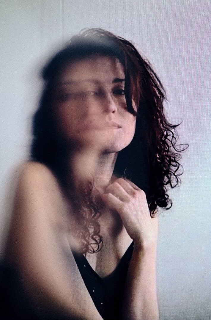 A thoughtful young person with dark hair gazes to the side, captured in soft black and white lighting.