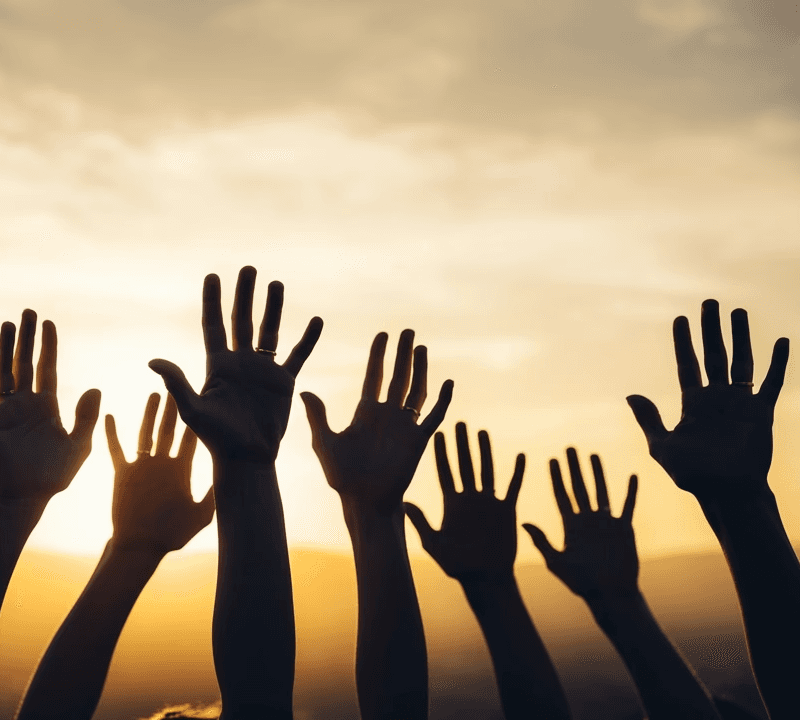 Viele erhobene Hände als Silhouetten gegen einen goldenen Sonnenuntergang – Symbol für Gemeinschaft und erfolgreich abgeschlossene Hilfsprojekte.