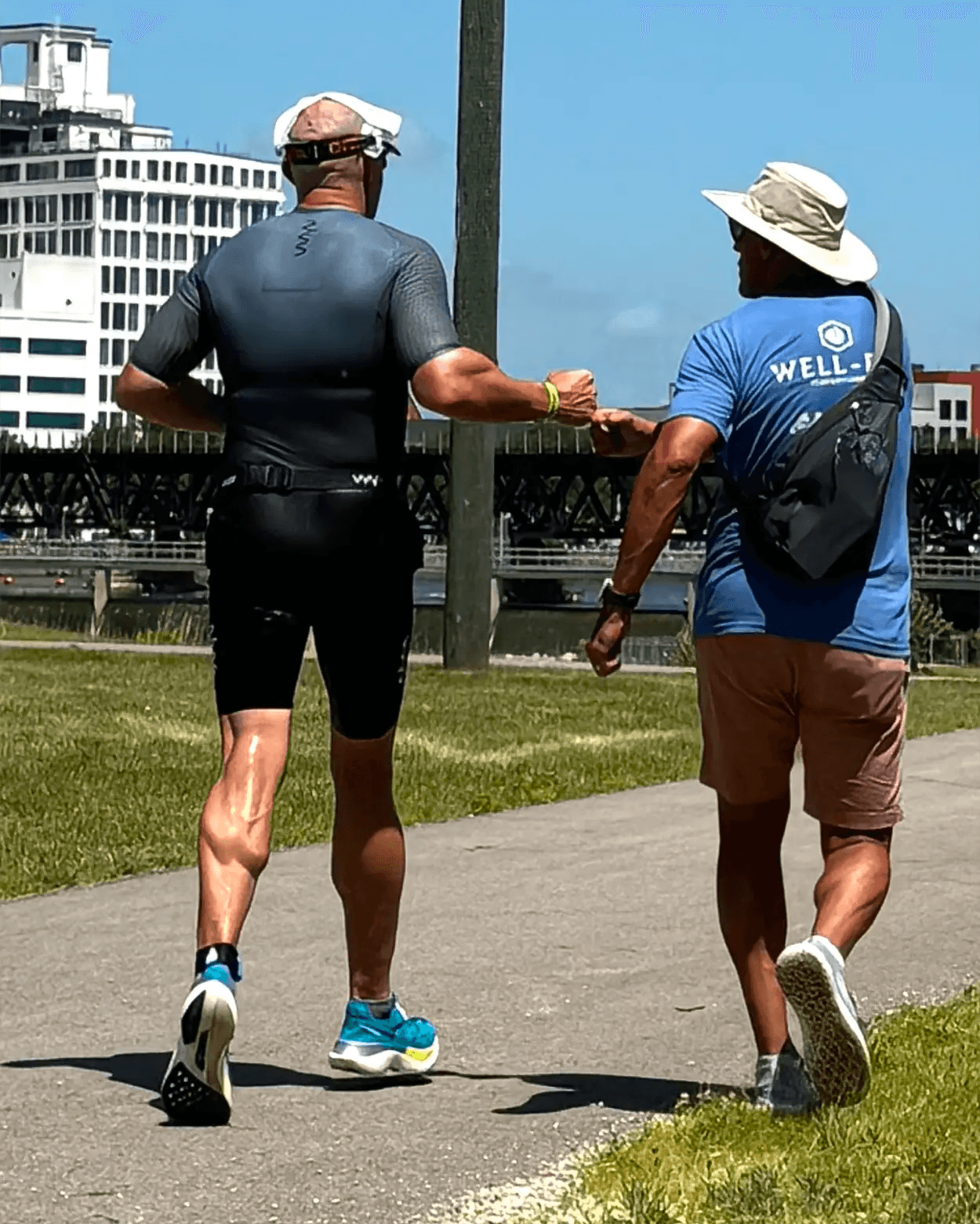 Well-Fit online triathlon coach Sharone Aharon running alongside an athlete on a Chicago riverfront path, fist-bumping in encouragement