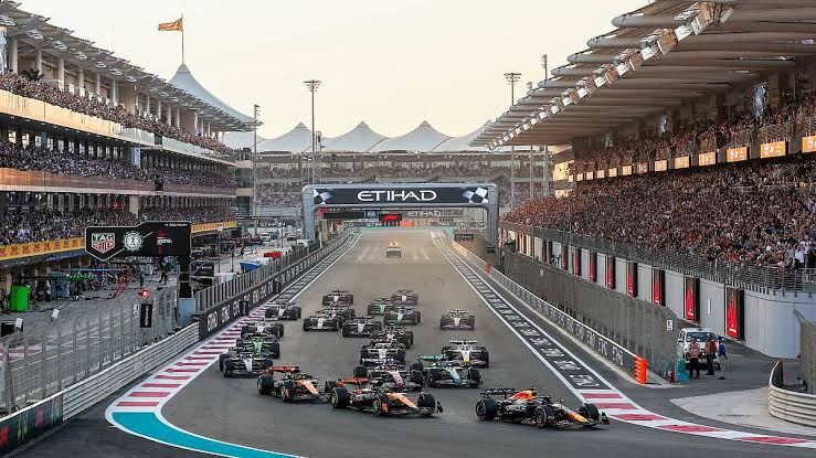 Formula 1 cars at the start of a race at Yas Marina, between the grandstands.