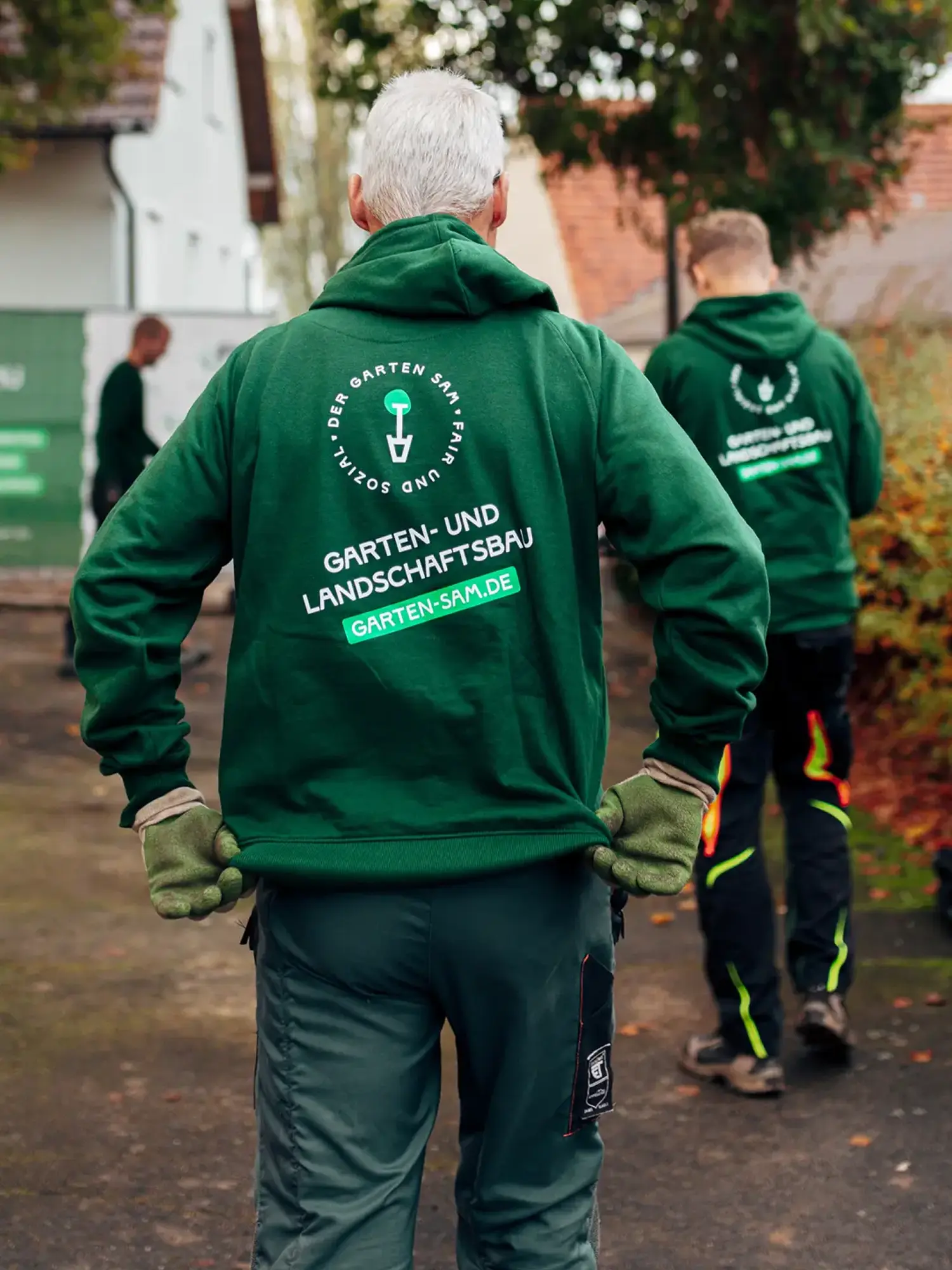 Mitarbeiter in grüner Arbeitskleidung mit Logo auf dem Rücken