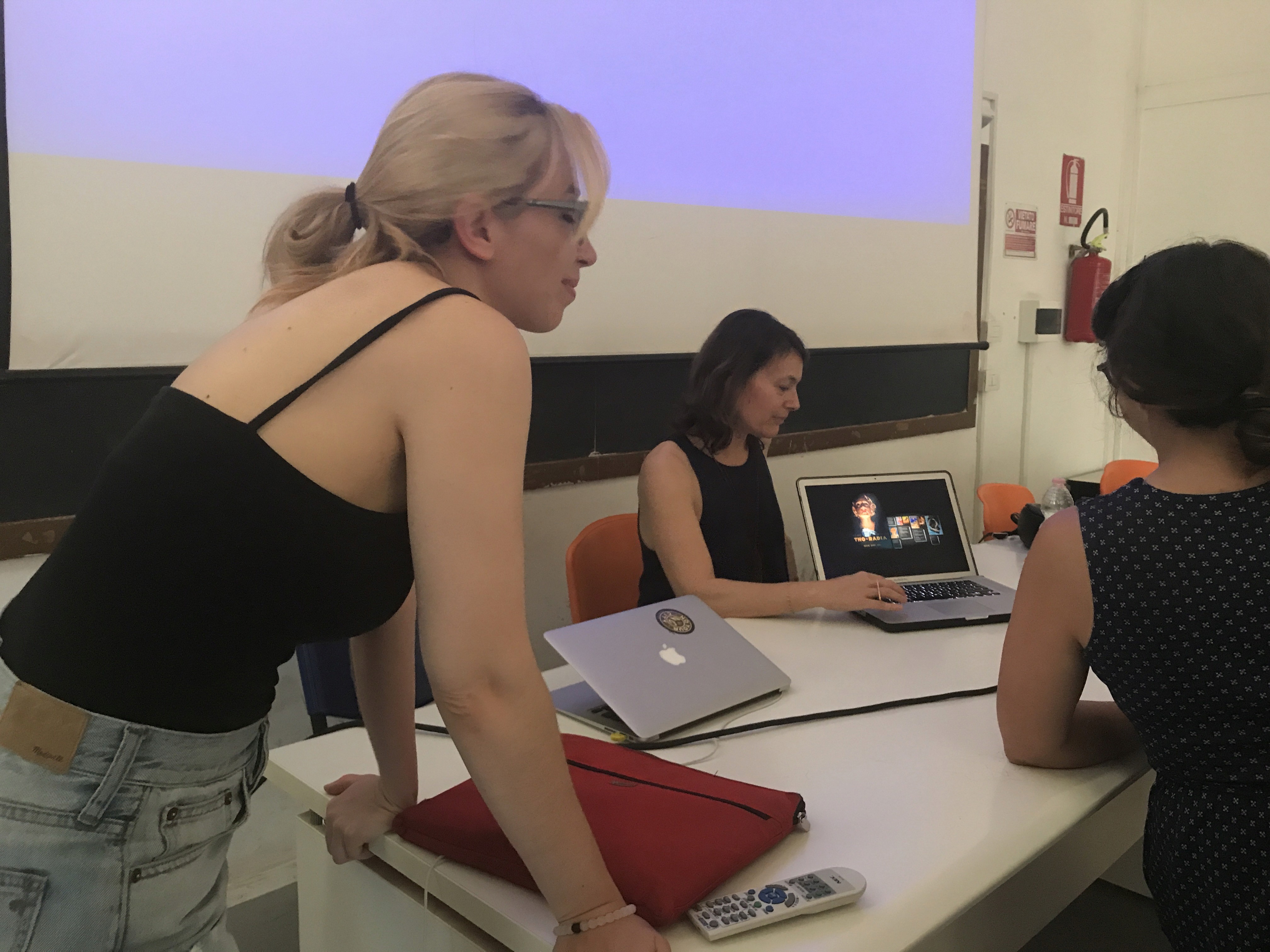 A photography of three women looking at a laptop in an conference room.