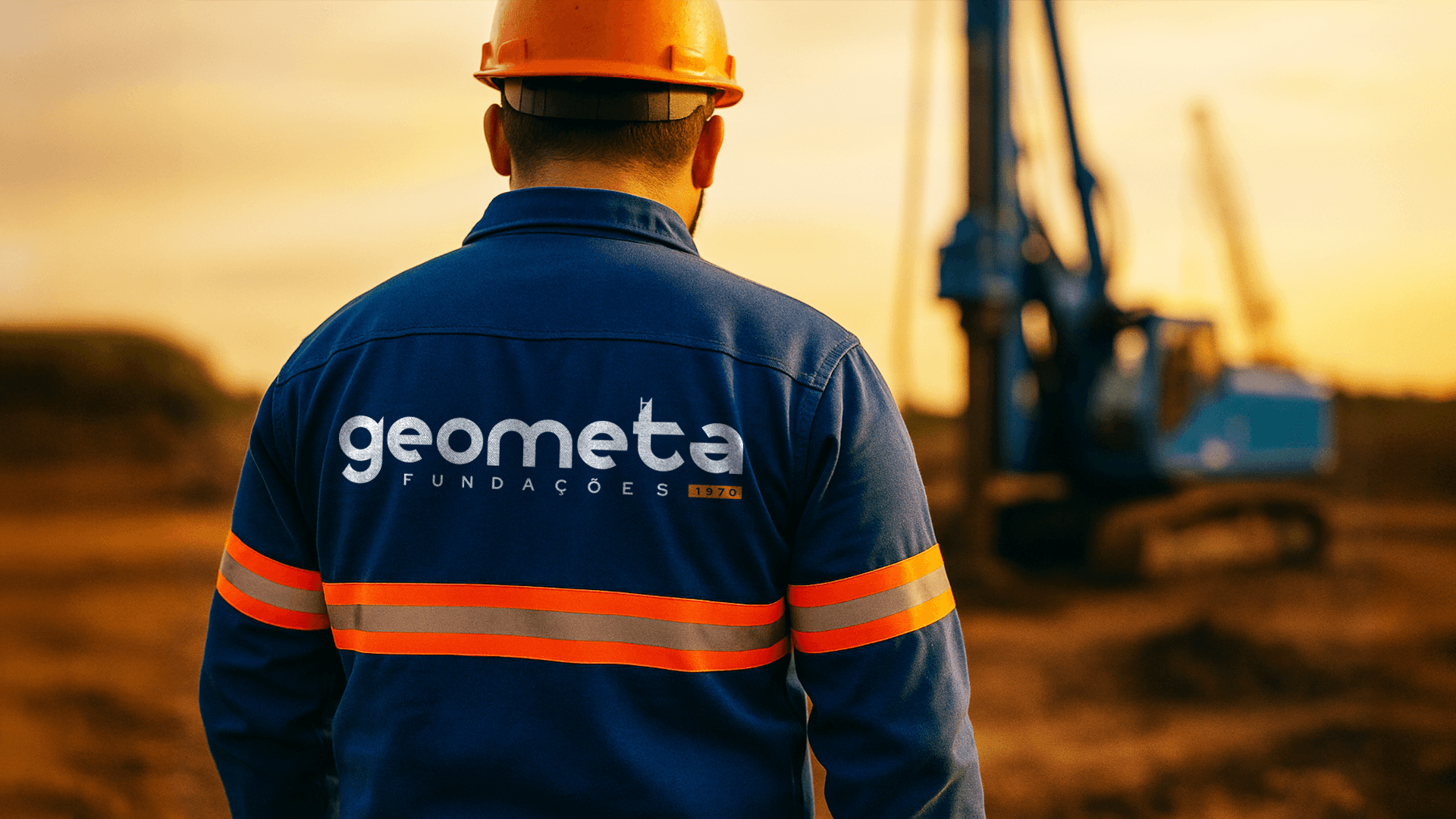 Colaborador em canteiro de obras com uniforme azul com a nova marca da Geometa e capacete, com perfuratriz ao fundo, representando operação de engenharia de fundações.