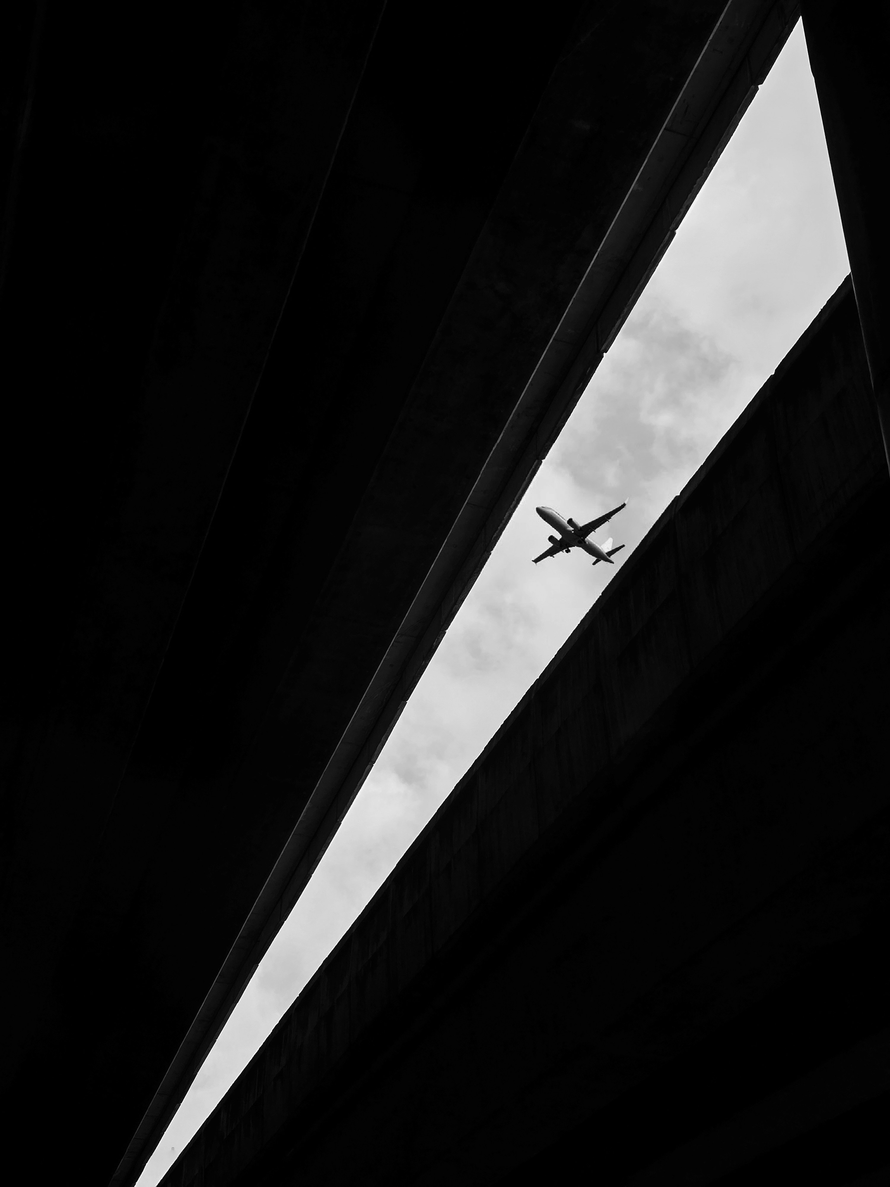 Airplane flies between two dark, angled structures.