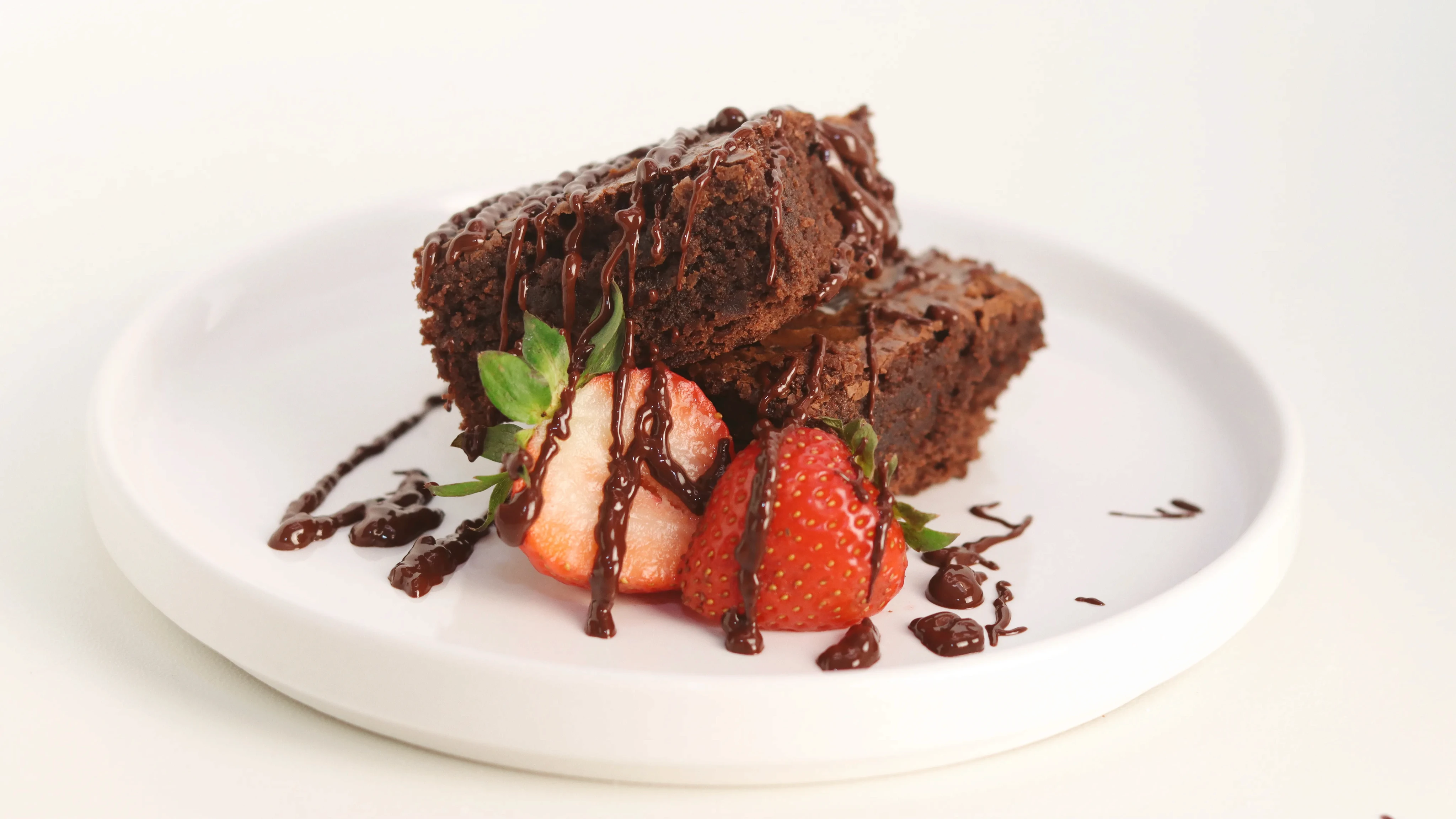 Brownies con fresas y chocolate derretido en plato blanco