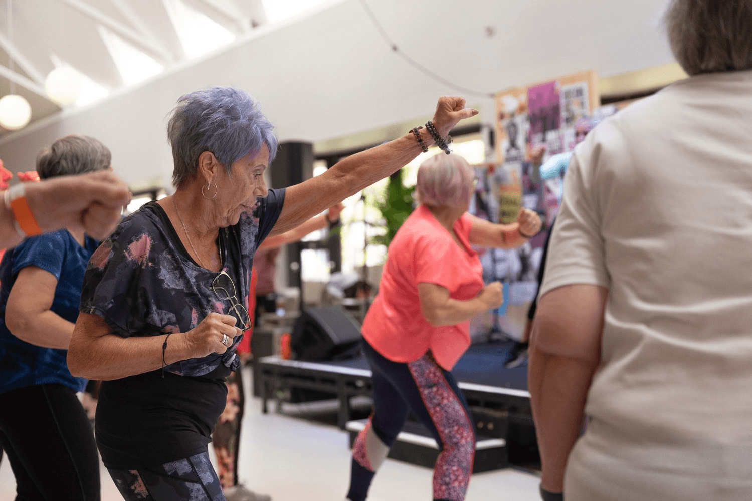 Older adults dance together in a bright hall during a group exercise class.
