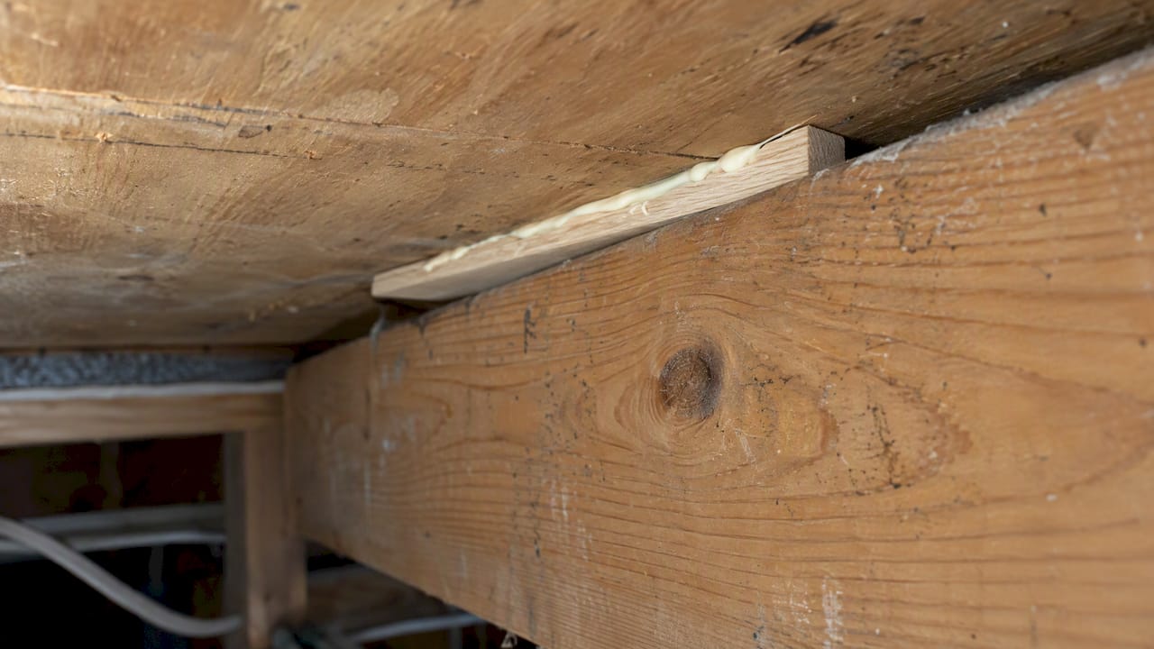 Adhesive-coated shim filling a floor joist gap