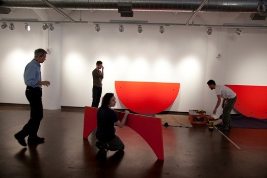 people installing a red rounded table in the designer as exhibition gallery