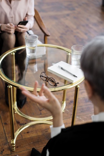 A photo of a two people conversing while sitting on chars with glass table between them