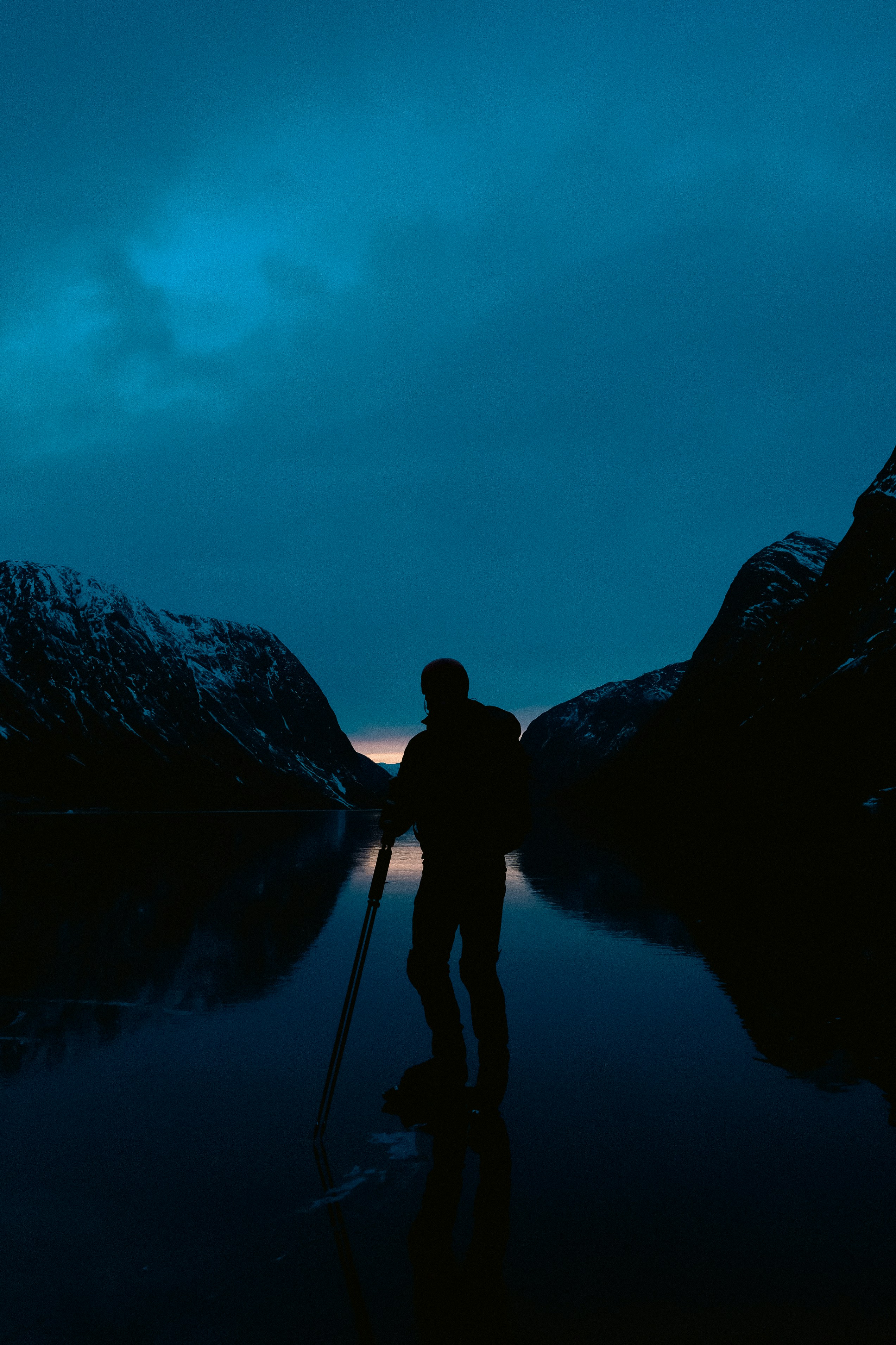 Silhouette of person standing on frozen lake at dusk