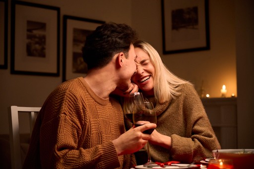 Couple smiling and holding hands across a table in a warmly lit room.