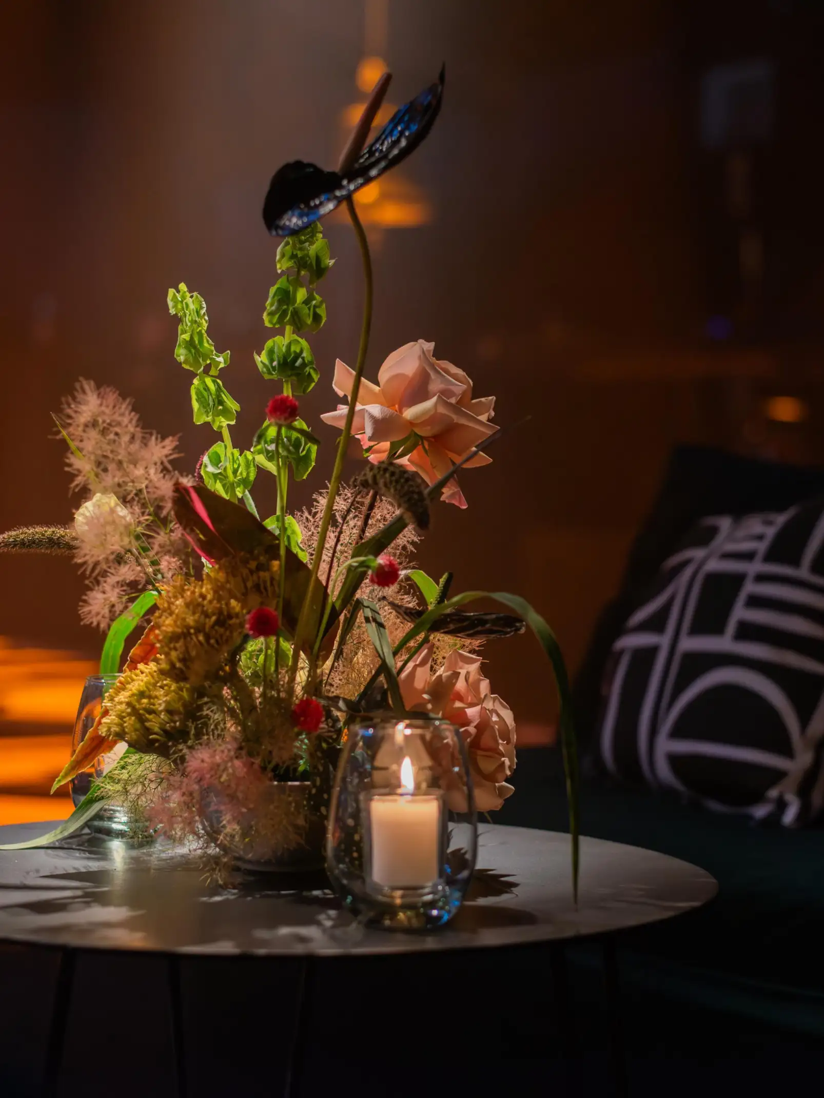 Centro floral sobre mesa auxiliar con velas, en ambiente íntimo y cálido con luz ambiental dorada.