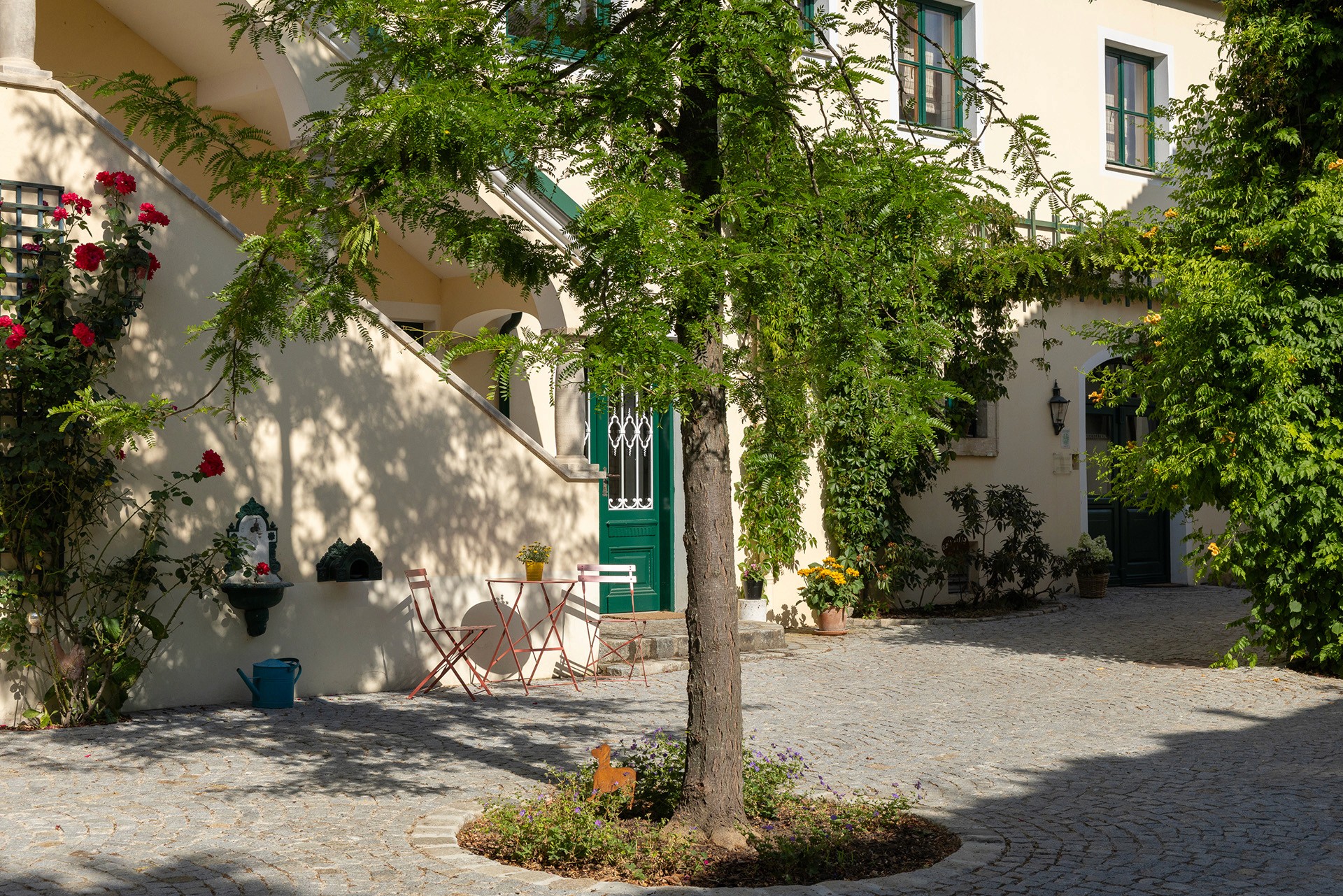 Innenhof eines Weinguts mit gepflanztem Solitärbaum, Sitzplatz und mediterraner Atmosphäre.