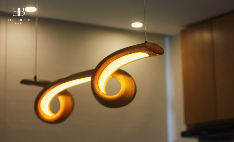 Close-up of the unique, curved wooden pendant light fixture hanging in the Echo Beach Suite, a stylish accommodation in Canggu, Bali.