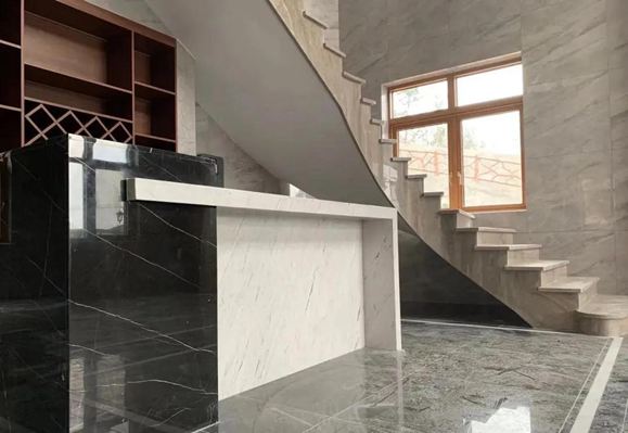 A reception area featuring a black and white marble desk and a curved marble staircase in a modern interior. The polished marble surfaces reflect the elegance of the contemporary design.