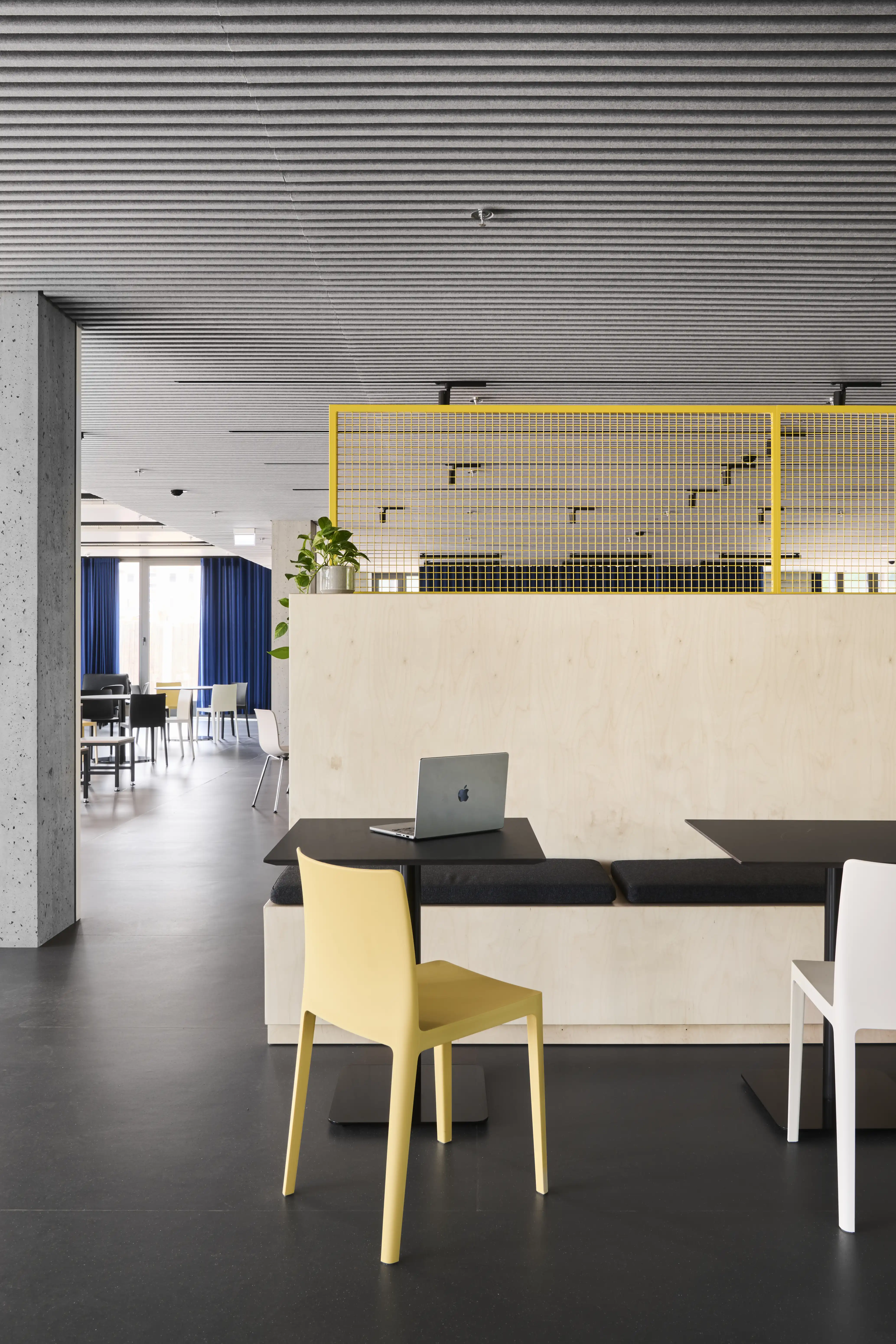 Work bench at ENPAL built into a birch tribune with black upholstered seating, a black table with laptop, a pale yellow chair and a yellow mesh railing above.
