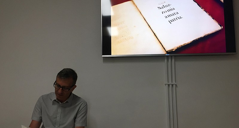 A photography of a man and behind him a screen that shows an old book.