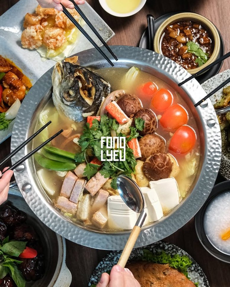 A vibrant table setting showcasing an assortment of Taiwanese dishes, including a clay pot soup with fish, tofu, and vegetables, alongside plates of fried shrimp, chicken, and rice, all presented with chopsticks and garnished with herbs.