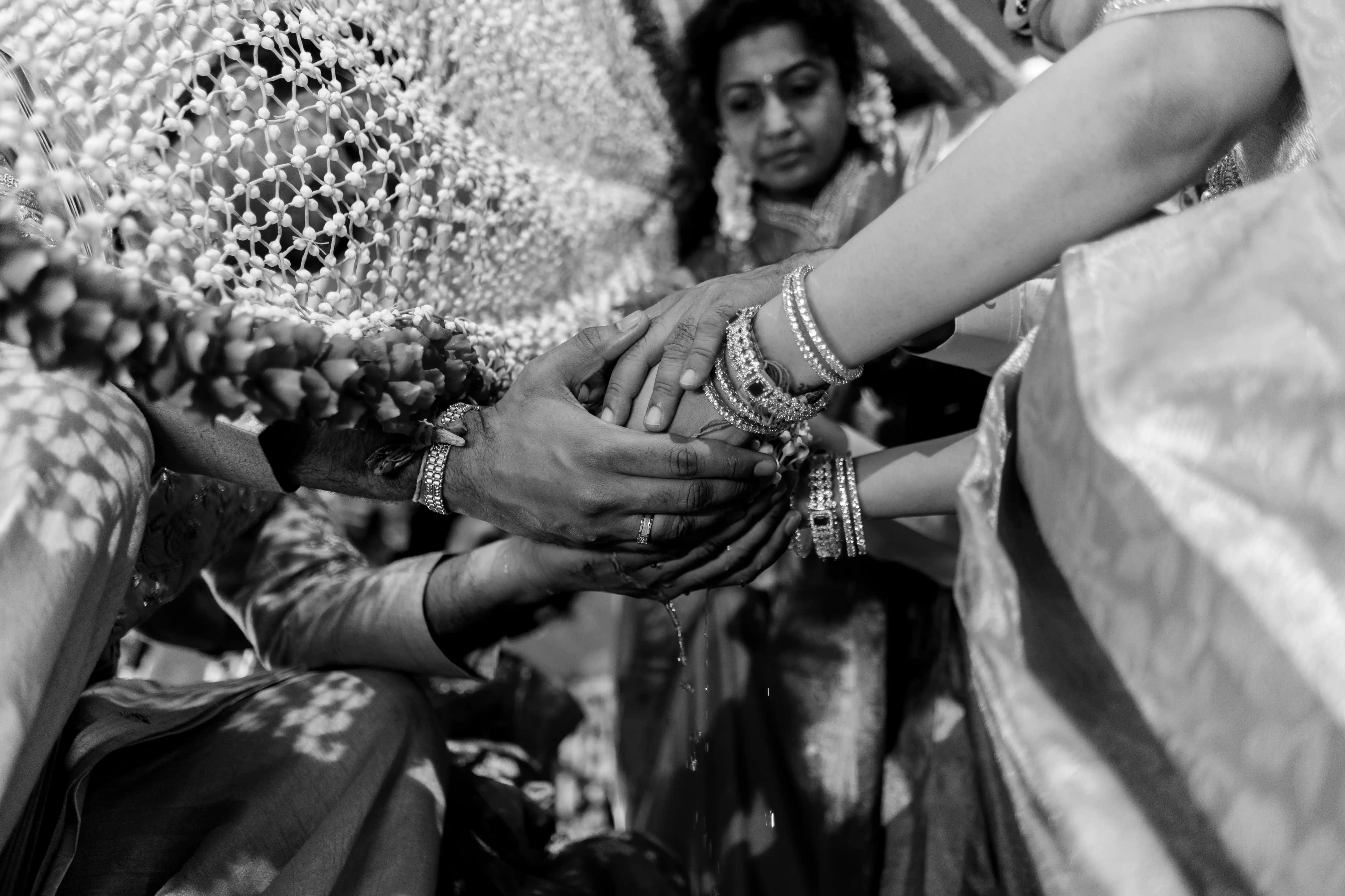 A black and white image of a bride and groom engaged in a hand-holding ritual captured by Out of The Blues Fine Art Wedding Photography in Hyderabad.