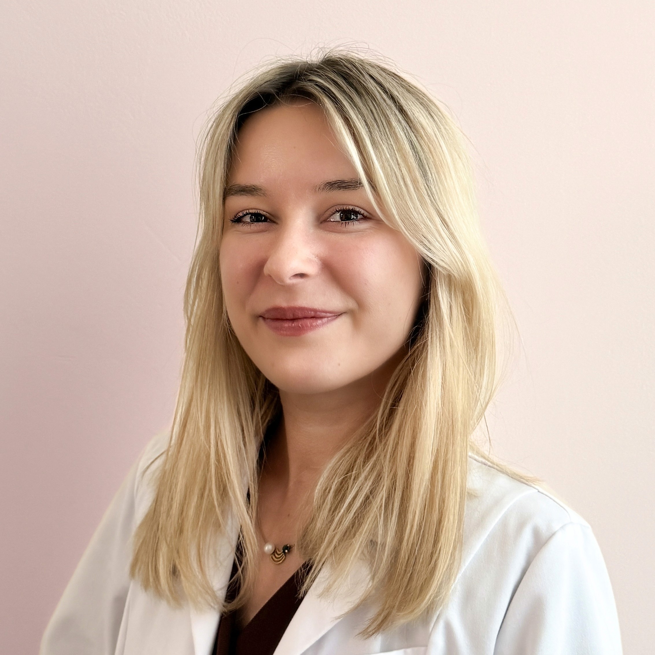 Portrait of Dr. Louise Cuveele, aesthetic doctor and founder of Cuveele's Clinic, wearing a white coat and smiling at the camera.