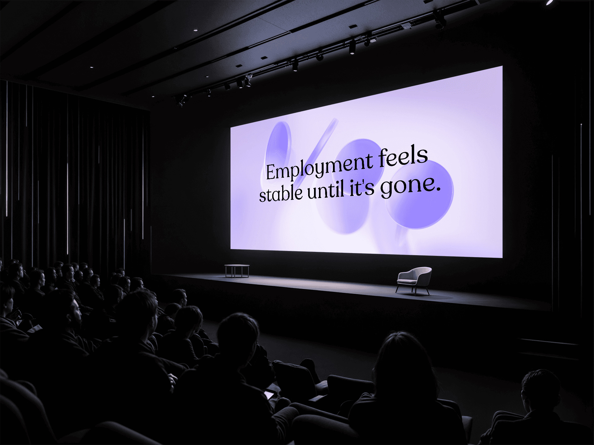 A dark auditorium with an audience facing a large screen displaying the message “Employment feels stable until it’s gone,” reflecting uncertainty in today’s job market and career stability.