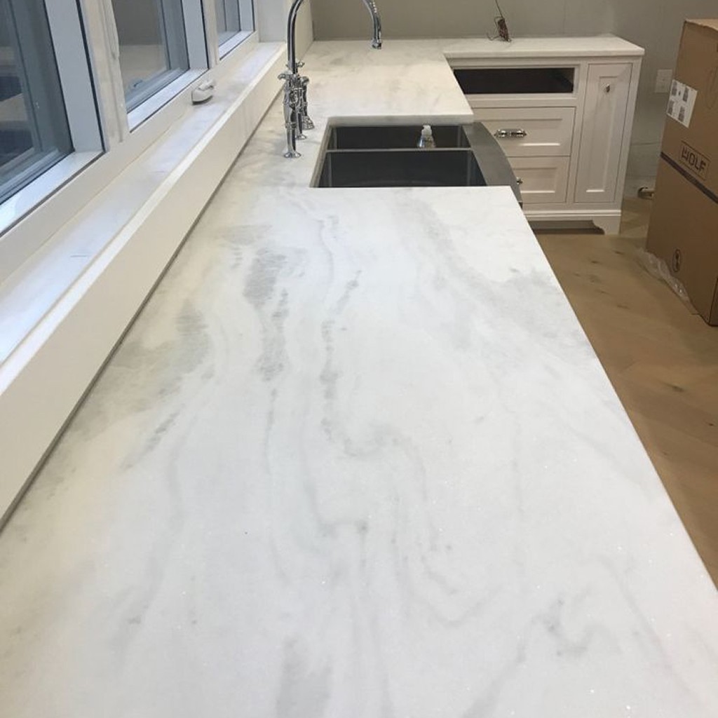 Bianco Tesoro dolomite marble kitchen countertop in soft white with light gray veining, a double sink and a Wolf appliance box in the background