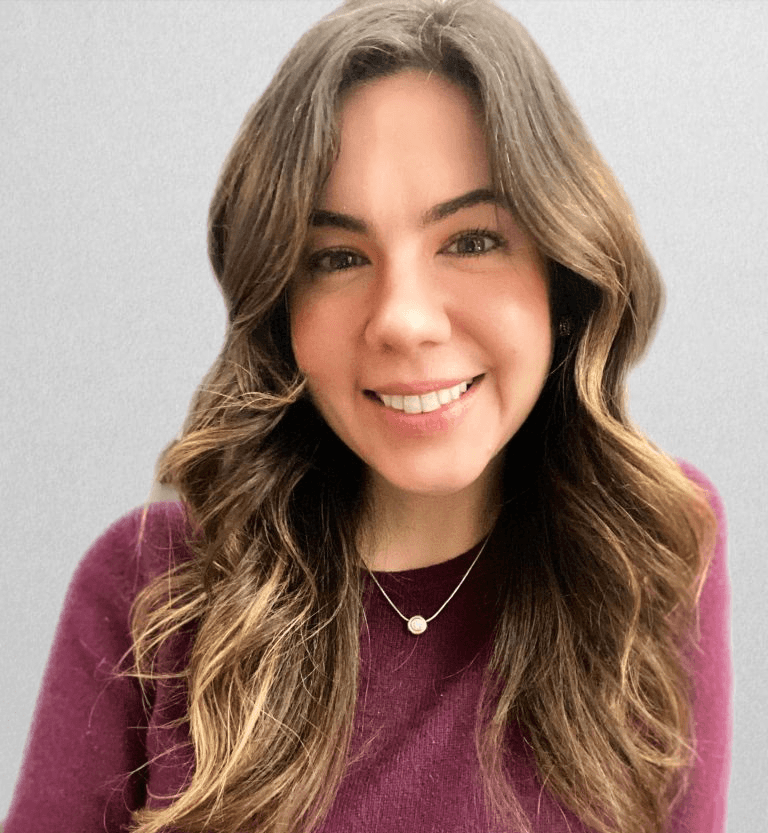 Rachel, a white woman with long, light brown hair and wearing a burgundy sweater is smiling at the camera
