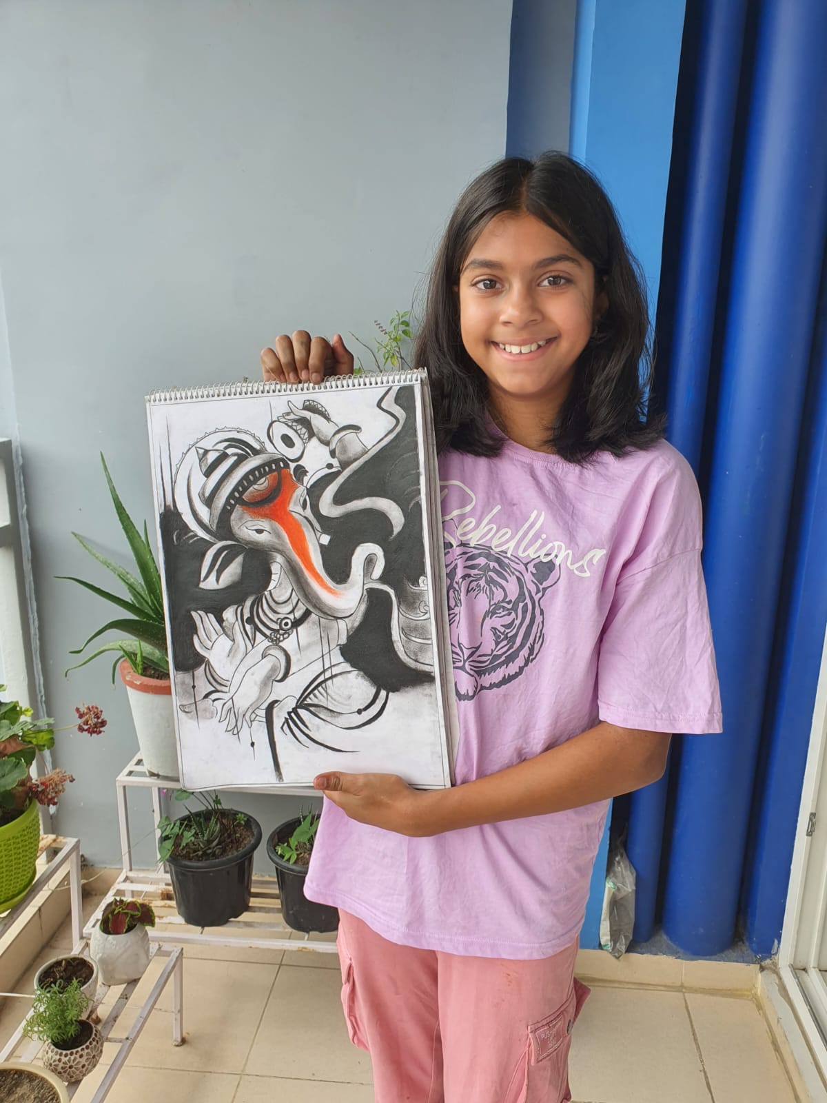 A smiling girl in a pink shirt holds a large artwork of the Hindu God Ganesh, standing in the Creative Pod studio.