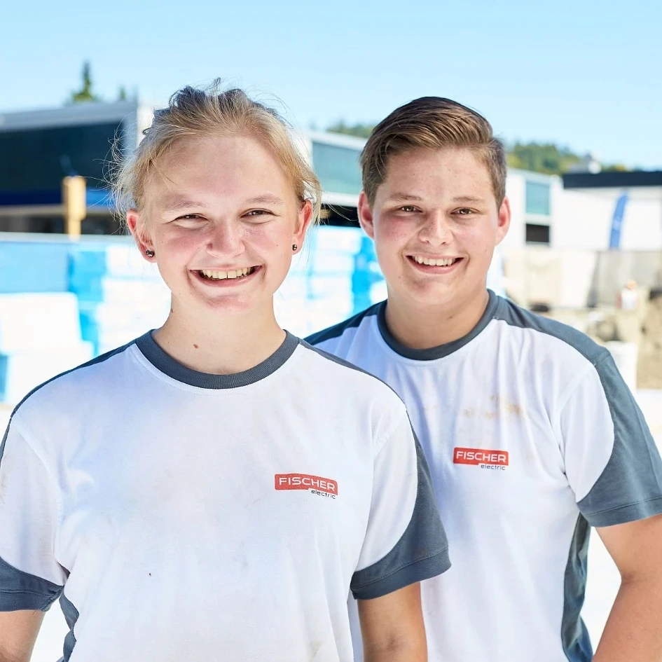 Deux jeunes collaborateurs portant des t-shirts de Fischer Electric se tiennent dehors devant un bâtiment